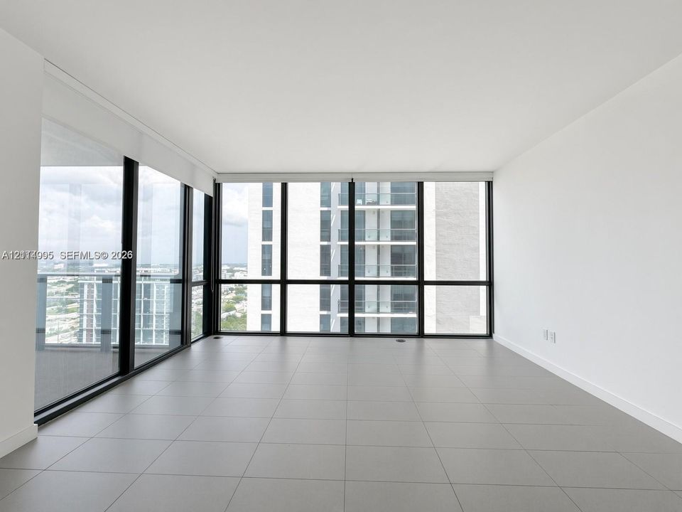 Floor-to-ceiling windows with black frames, expansive grey tile flooring, and neutral white wall finishes