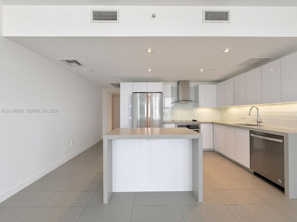 Kitchen featuring high-gloss white cabinetry, stainless steel appliances, stone-finish countertops, tile backsplash, and ceramic tile flooring