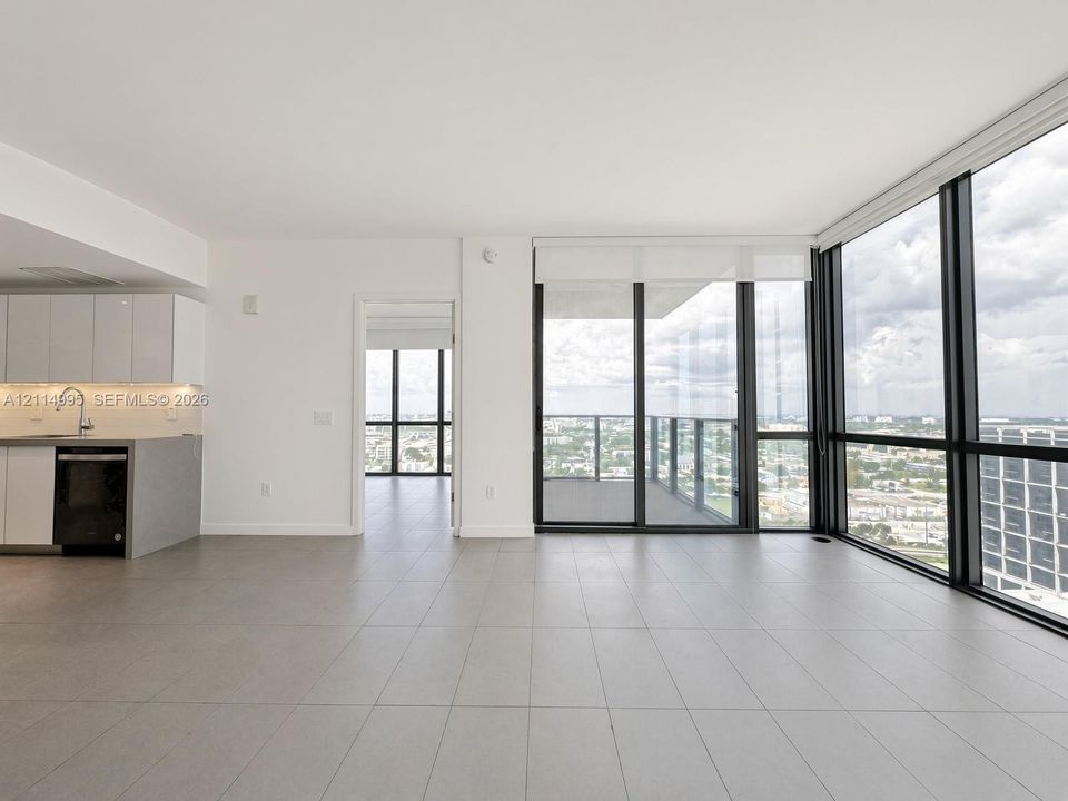 Open-concept interior featuring floor-to-ceiling glass windows, neutral tile flooring, private balcony access, and built-in cabinetry with integrated appliances