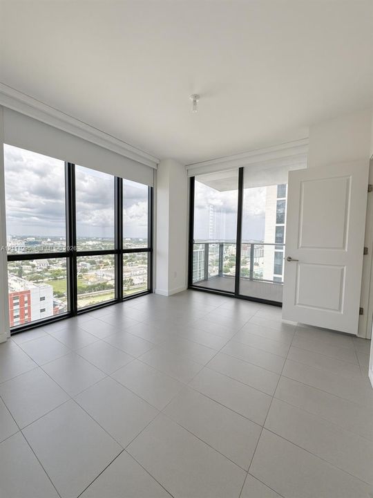 Floor-to-ceiling windows, large-format tile flooring, private balcony with metal railing, and neutral wall finishes