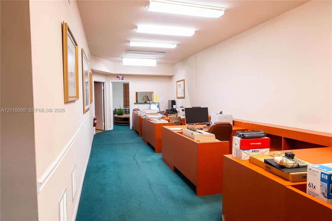 Interior workspace featuring linear fluorescent overhead lighting and fixed wooden-finish cabinetry with integrated desk surfaces