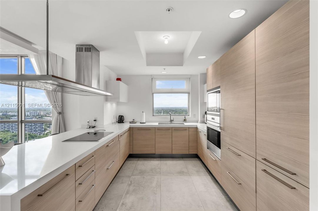 Kitchen featuring light-tone wood-finish cabinetry, white countertops, recessed lighting, a stainless steel range hood, and large-format tile flooring