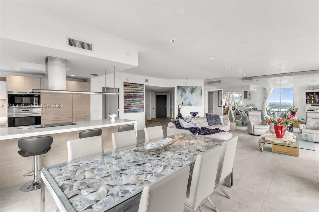 Open-concept kitchen featuring light wood-finish cabinetry, a white countertop island, and stainless steel wall-mounted oven and microwave