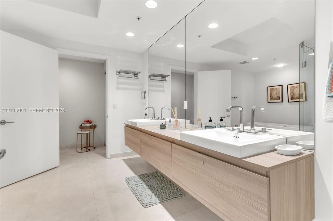 Floating wood-finish double vanity featuring integrated rectangular sinks, polished chrome faucets, and an expansive wall-mounted mirror