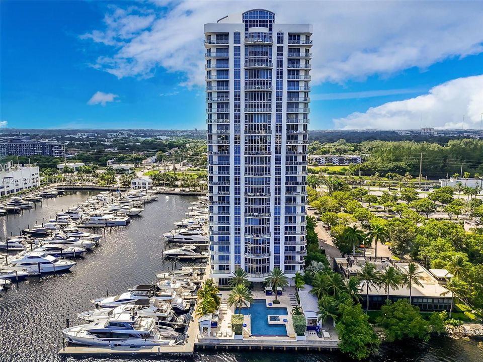 High-rise tower featuring extensive glass balcony railings, a ground-level swimming pool, and direct access to a private deep-water marina