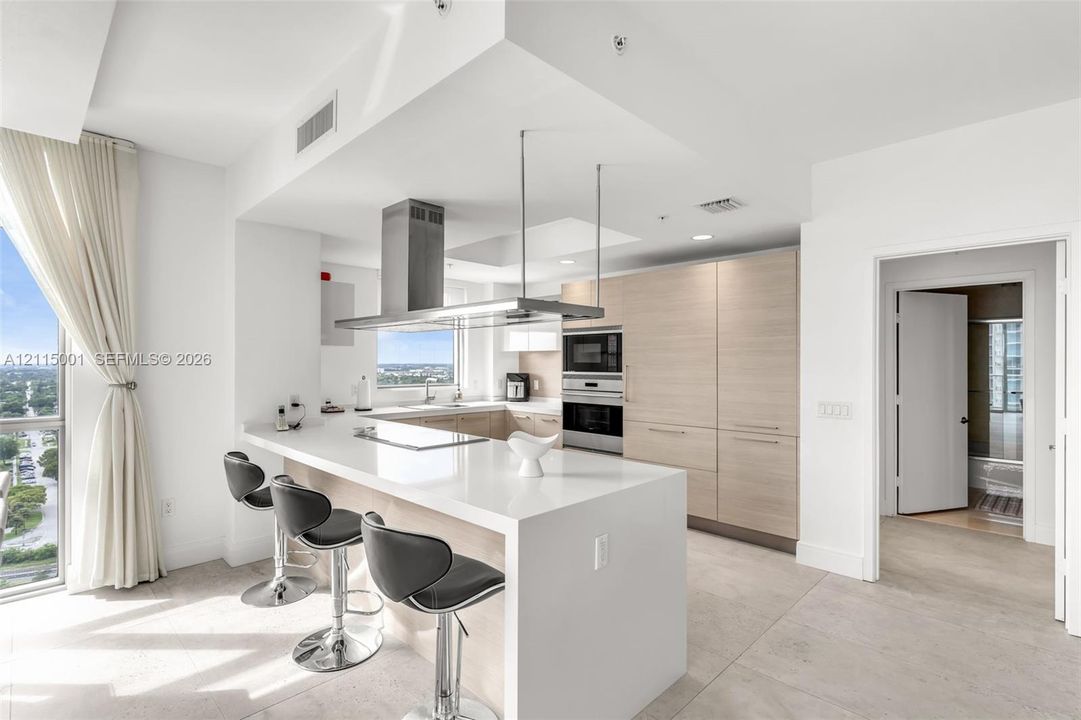 Kitchen featuring quartz countertops, flat-panel wood-finish cabinetry, stainless steel built-in oven and microwave, and a stainless steel suspended range hood