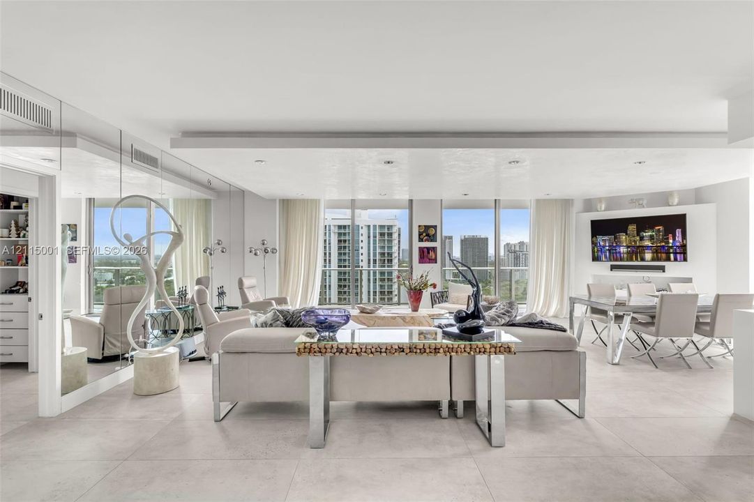 Open-concept living area featuring large-format tile flooring, floor-to-ceiling windows, a mirrored wall, and recessed tray ceiling lighting
