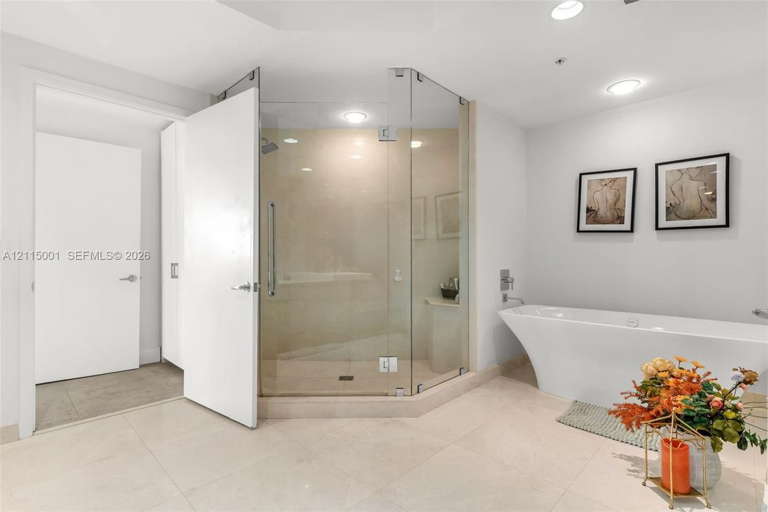Freestanding soaking tub with wall-mounted fixtures, frameless glass-enclosed shower, large-format tile flooring, and recessed ceiling lighting