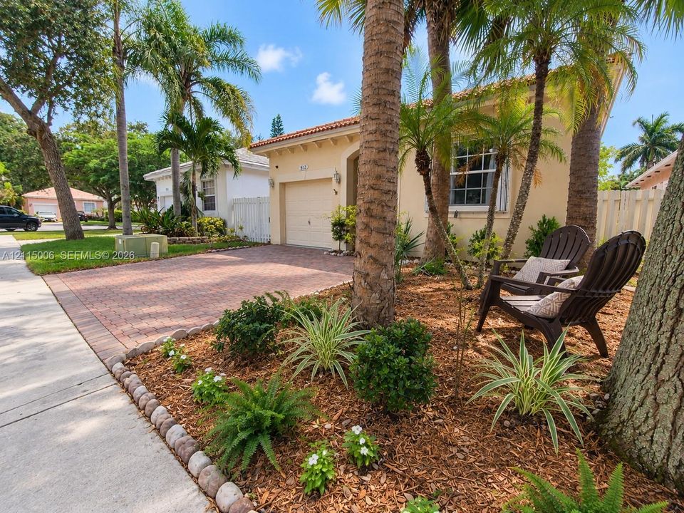 Stucco exterior featuring a tile roof, brick-paver driveway, single-car garage, and mulched landscaping with mature palm trees