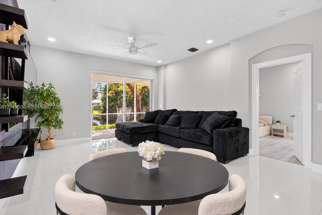 Living area featuring polished tile flooring, recessed lighting, a ceiling fan, wall-mounted display shelving, and sliding glass doors with a screen-enclosed patio