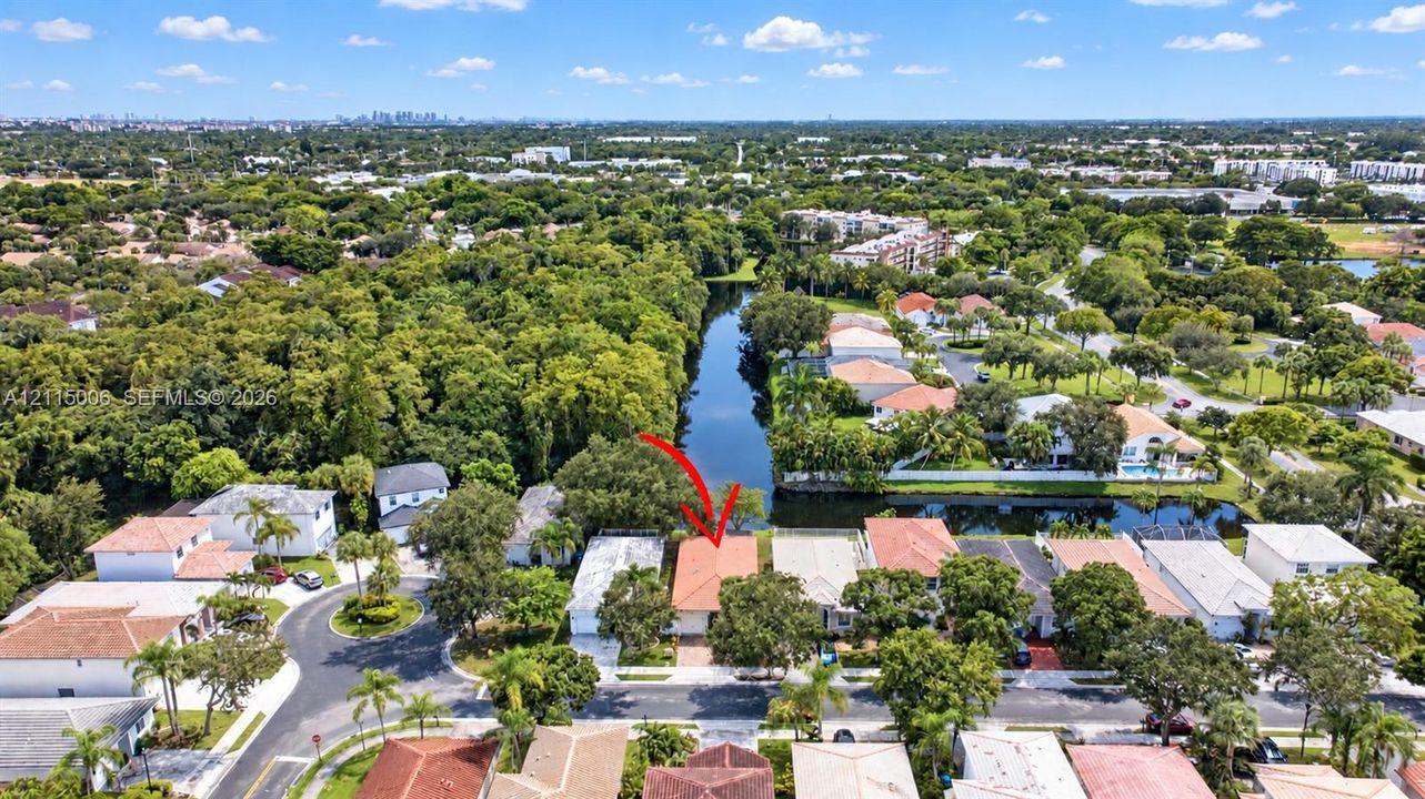 Aerial perspective of waterfront property featuring a tile roof, paved driveway, and established tree canopy