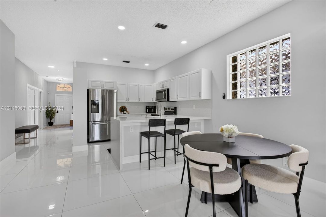 Kitchen featuring white cabinetry, quartz-surface countertops, stainless steel appliances, glass block window, and polished tile flooring