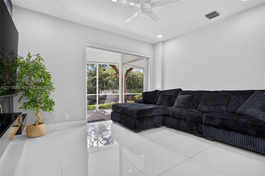 Large-format tile flooring, ceiling fan, and sliding glass doors opening to a screened lanai with exterior water feature
