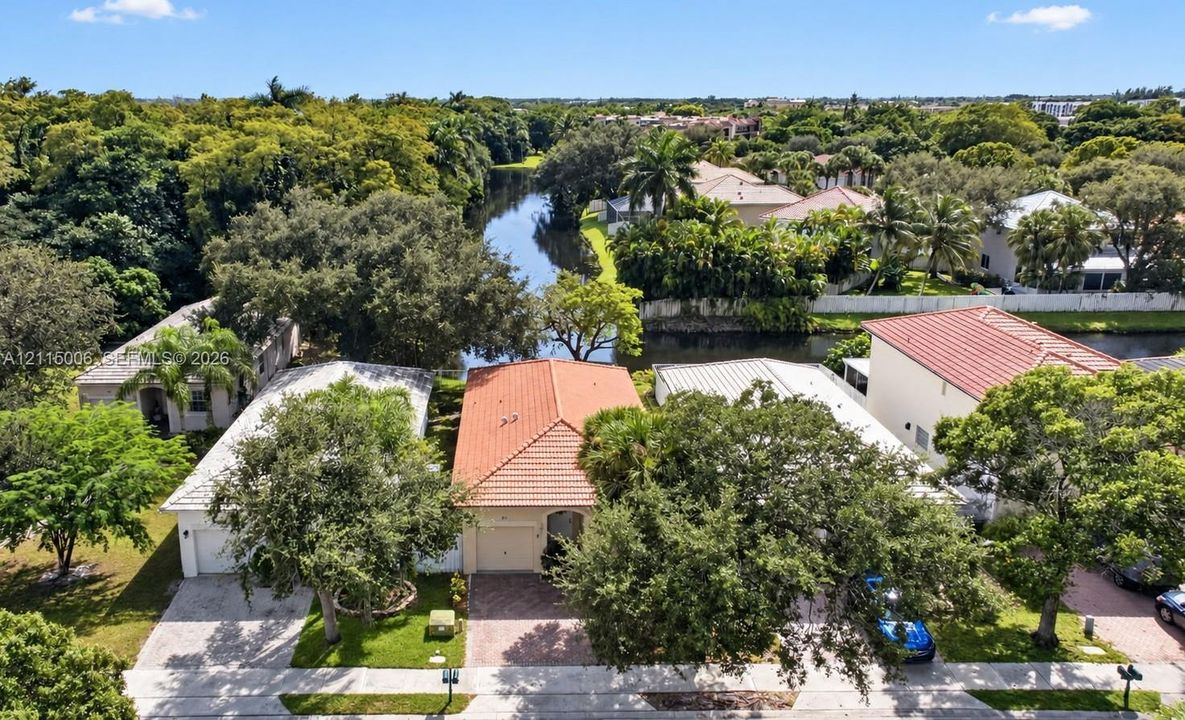 Aerial perspective featuring residences with terracotta-style roof tiles, paved driveways, and mature landscaping situated along a waterway