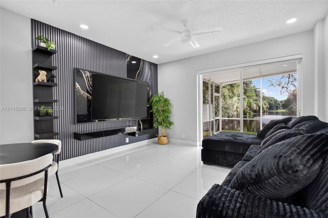 Accent wall featuring textured vertical paneling and integrated shelving, large-format tile flooring, recessed ceiling lighting, and sliding glass doors opening to a screened enclosure