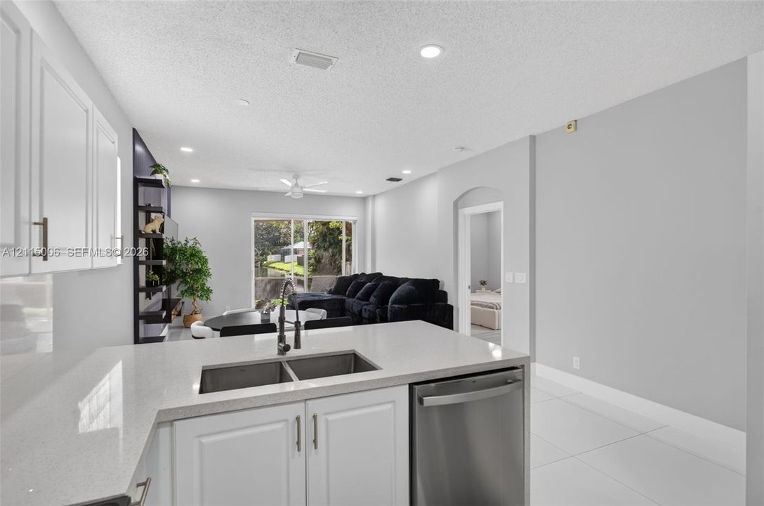 Kitchen featuring white cabinetry, solid-surface countertops, dual-basin stainless steel sink, and stainless steel dishwasher, complemented by tile flooring throughout