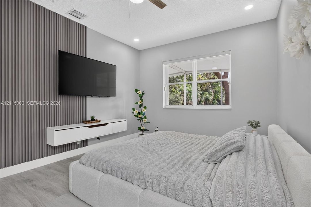 Room featuring wood-finish flooring, a charcoal-toned vertical slat accent wall, a white wall-mounted floating media console, and a large multi-pane window
