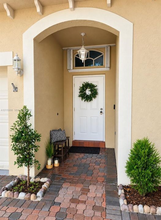 Covered entryway featuring a recessed arched opening, decorative window, pendant lantern fixture, and multi-tonal paver hardscaping