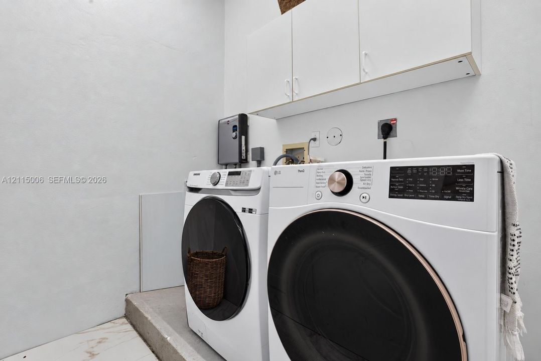 Laundry area featuring white wall-mounted cabinetry and large-format tile flooring