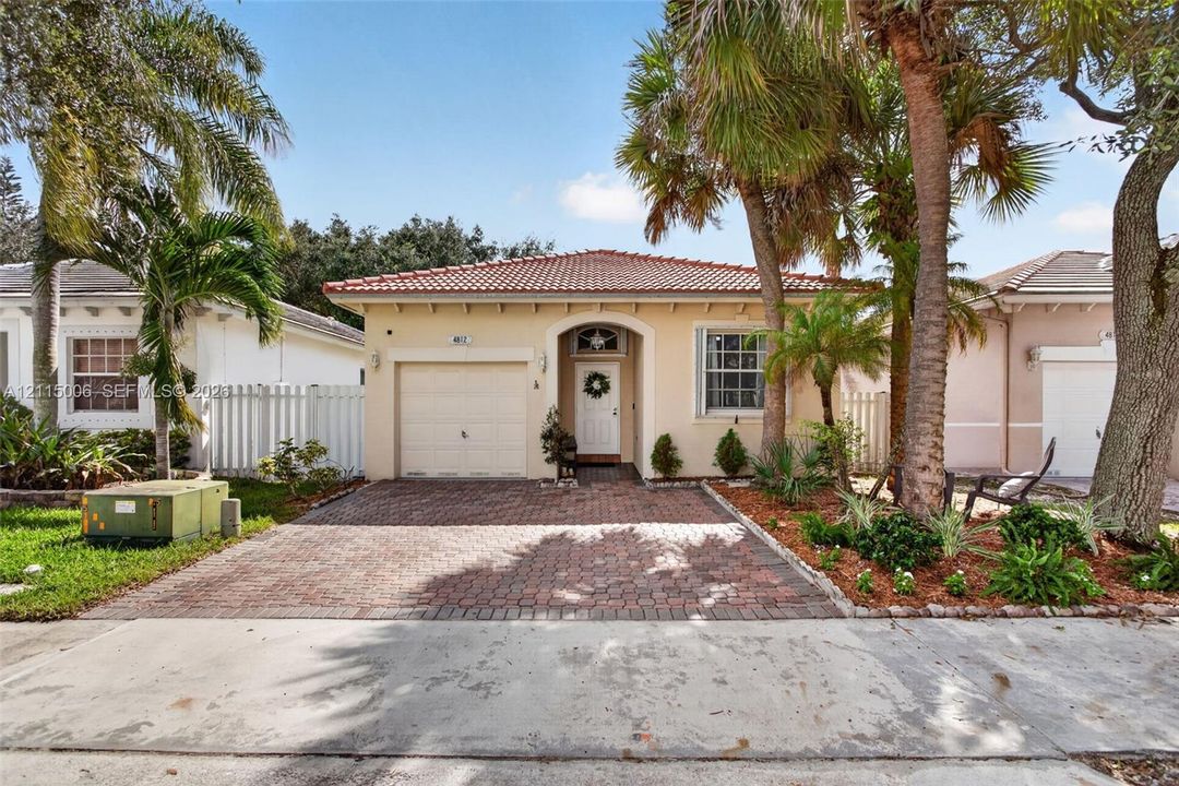 Single-story residence featuring a tile roof, paver driveway, arched entryway, and mature palm trees
