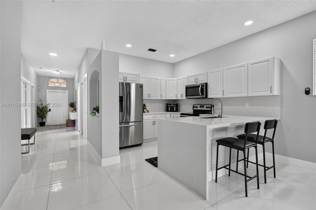Kitchen featuring white cabinetry, solid surface countertops, stainless steel appliances, a peninsula with seating space, and polished tile flooring
