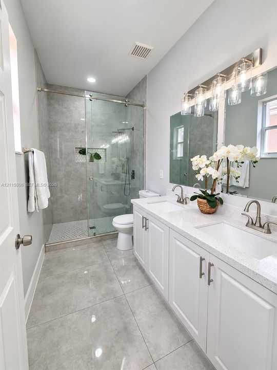 Double vanity featuring white shaker-style cabinetry, quartz countertops, and dual undermount sinks, complemented by a walk-in shower with a glass enclosure, floor-to-ceiling tile surround, and polished nickel fixtures