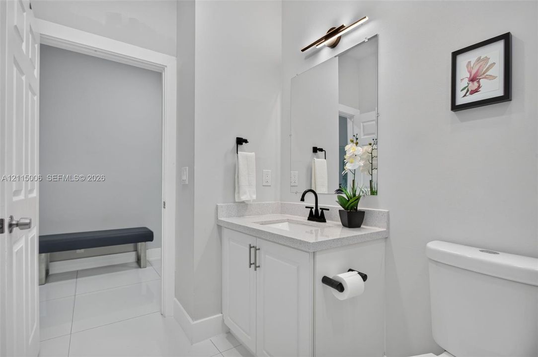 Bathroom featuring a white vanity with a composite stone countertop, rectangular undermount sink, matte black faucet, and linear LED wall-mounted light fixture