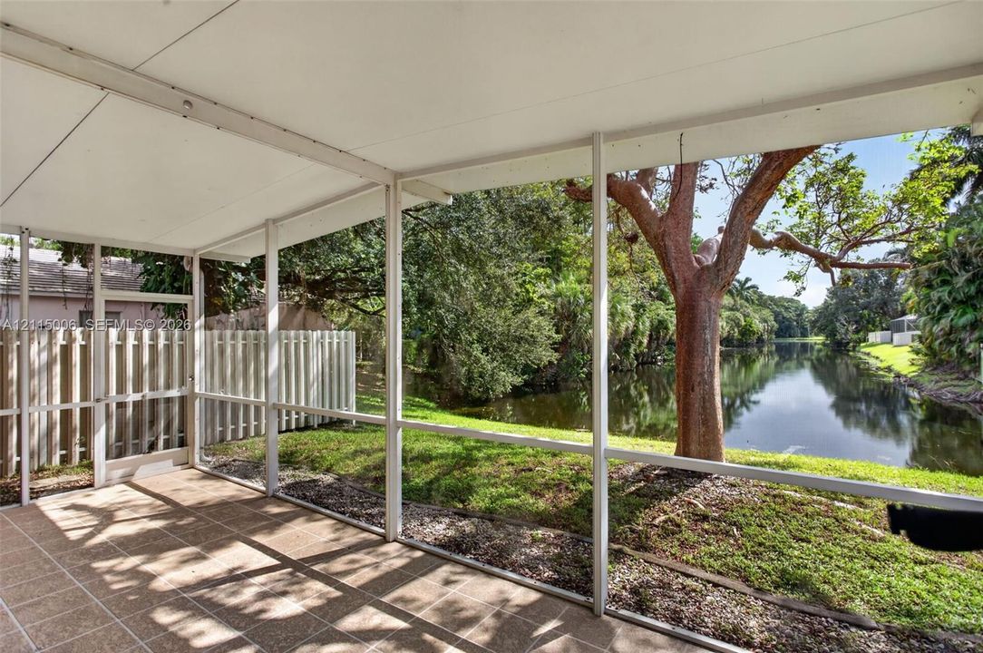 Screened-in patio with tile flooring and white structural frame overlooking a water feature and mature landscaping