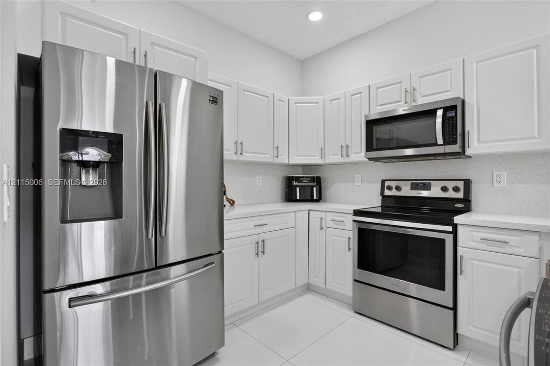 Kitchen featuring white shaker-style cabinetry, stainless steel refrigerator, over-the-range microwave, electric range, and light-toned solid surface countertops