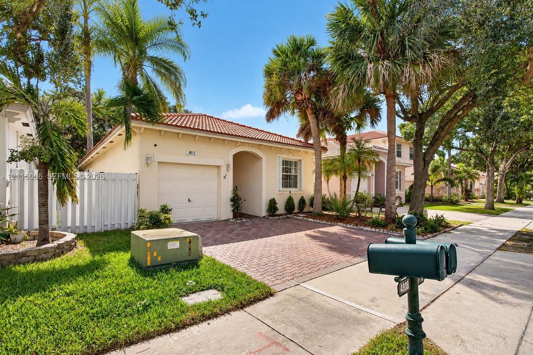 Single-story residence featuring a barrel-tile roof, paved driveway, attached garage, and white privacy fencing