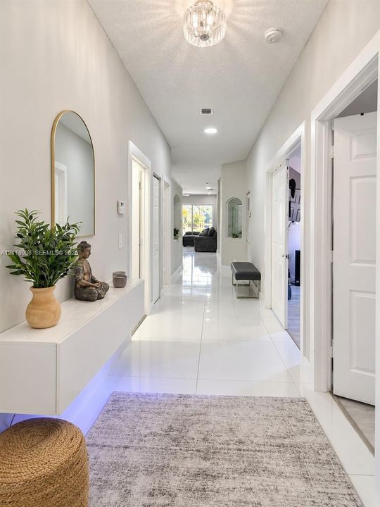 Hallway featuring large-format tile flooring, a wall-mounted floating console, an arched wall mirror, and a decorative flush-mount ceiling fixture
