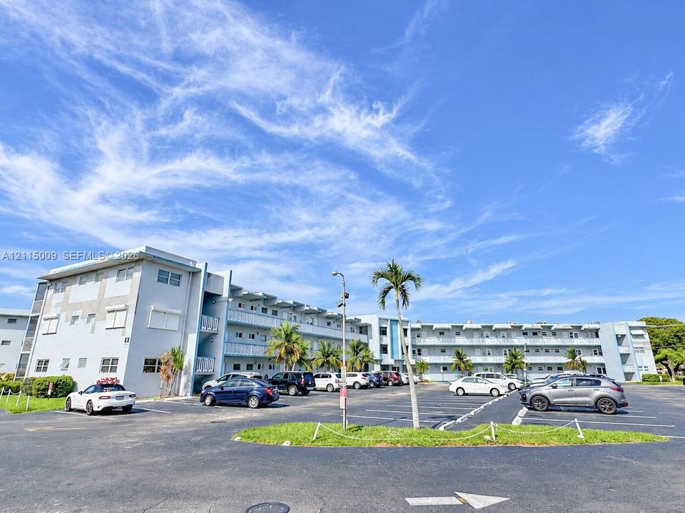 Multi-story exterior featuring concrete masonry construction, expansive paved parking area, and mature palm landscaping