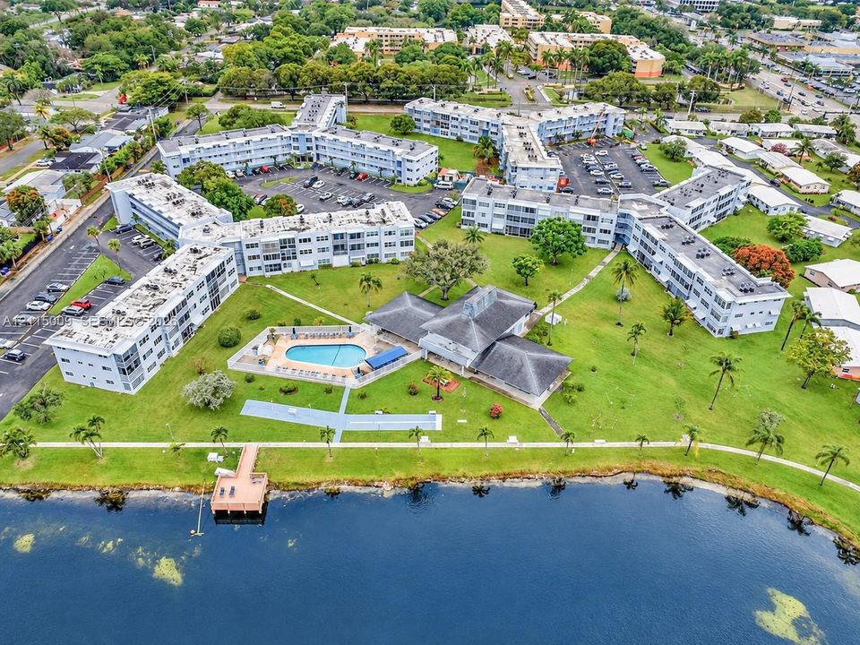 Aerial perspective of the residential complex featuring a swimming pool, waterfront bulkhead with deck, expansive lawn, and paved parking areas