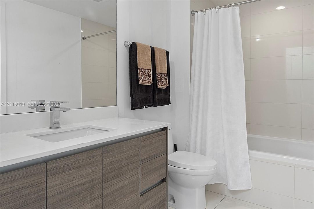 Bathroom featuring a flat-panel wood-finish vanity, rectangular undermount sink, stone-surface countertop, chrome single-handle faucet, and full-height tiled shower surround