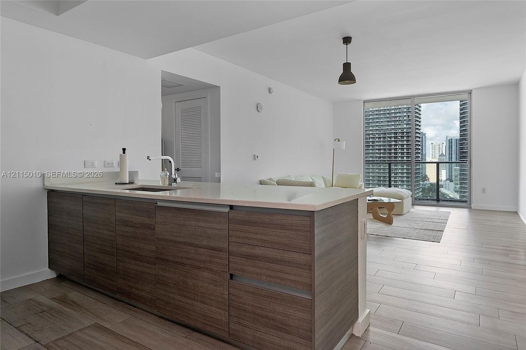 Kitchen island featuring wood-finish cabinetry, solid-surface countertop, and an undermount sink, complemented by light-toned tile flooring and expansive sliding glass doors