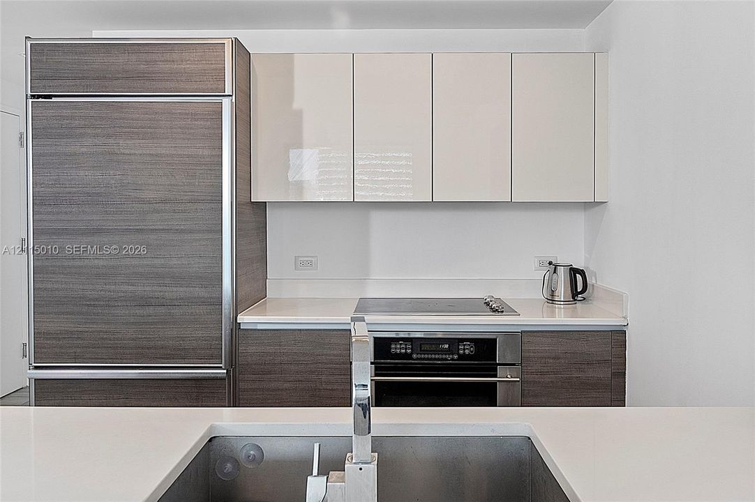 Kitchen featuring high-gloss cabinetry, wood-finish paneling, an integrated refrigerator, a built-in oven with a cooktop, and an undermount sink with a chrome faucet