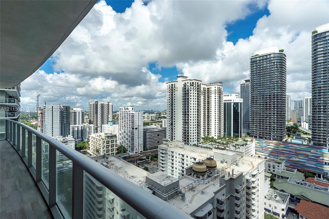Private balcony with glass panel railing and tile flooring overlooking an expansive urban skyline