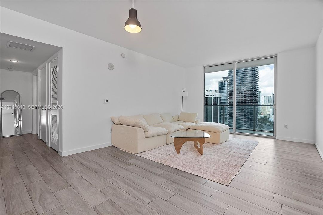 Wood-finish flooring, floor-to-ceiling glass sliding doors, private balcony with metal railing, and pendant lighting