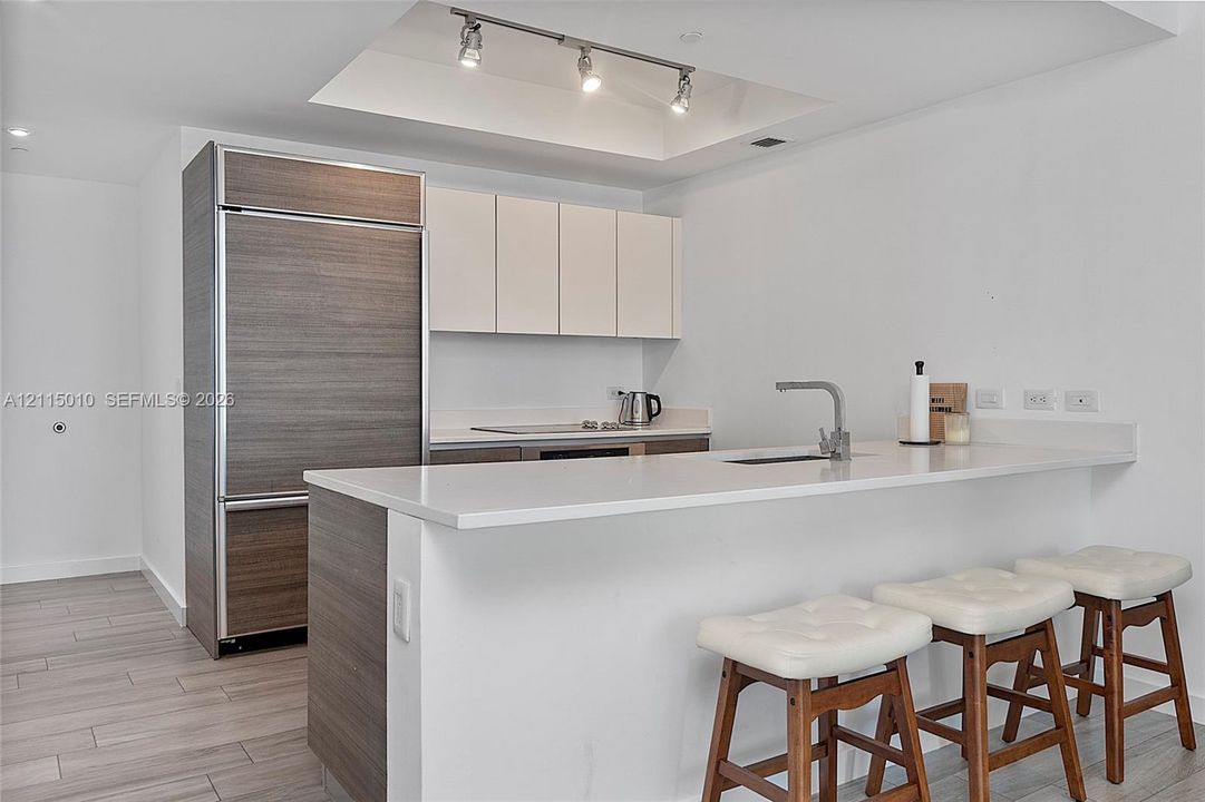Kitchen featuring a stone-surface island with an integrated sink, custom cabinetry with wood-finish paneling, a paneled refrigerator, recessed ceiling lighting, and wood-finish flooring