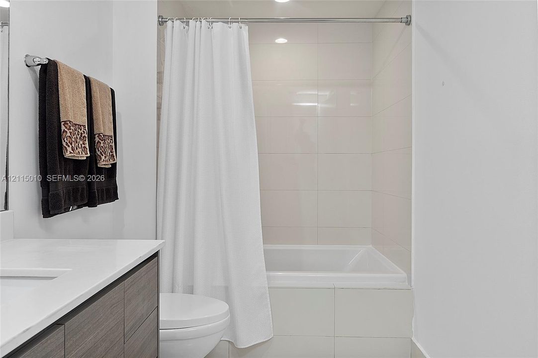 Bathroom featuring a floating vanity with stone countertop, recessed lighting, and a tub with large-format wall tile surround