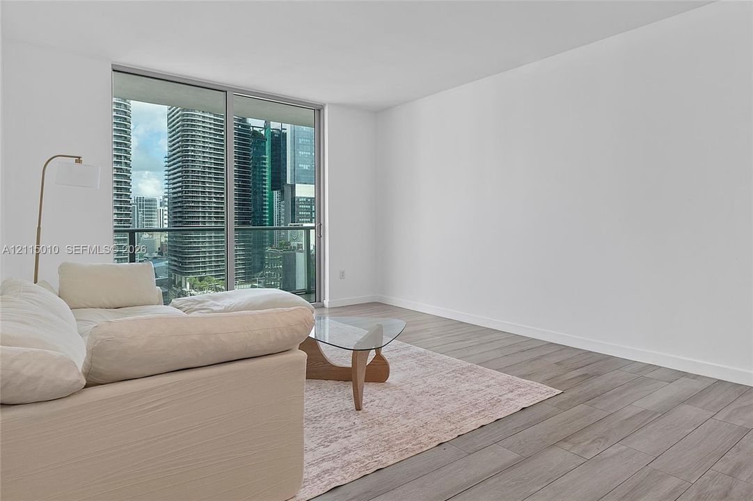 Floor-to-ceiling sliding glass doors, urban skyline backdrop, and wood-finish flooring