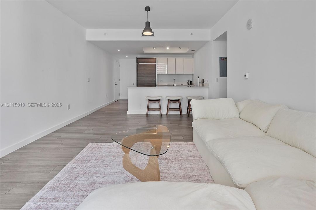 Open-concept interior featuring wood-finish flooring, a kitchen island with stone countertops, modern flat-panel cabinetry, and a minimalist pendant light fixture