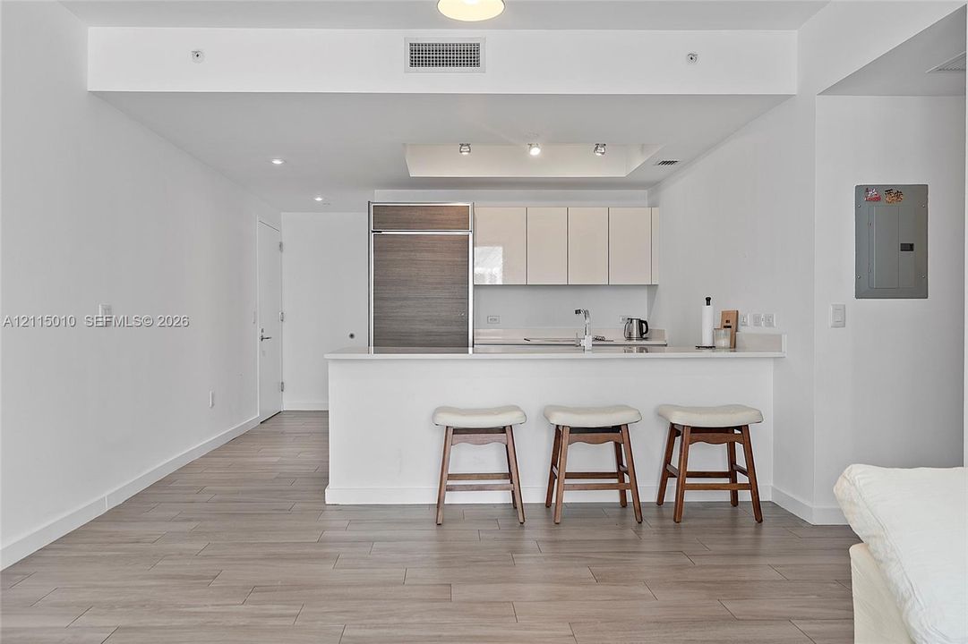 Kitchen featuring flat-panel cabinetry, wood-finish paneling on a built-in refrigerator, stone-surface countertop, recessed ceiling lighting, and wood-finish flooring