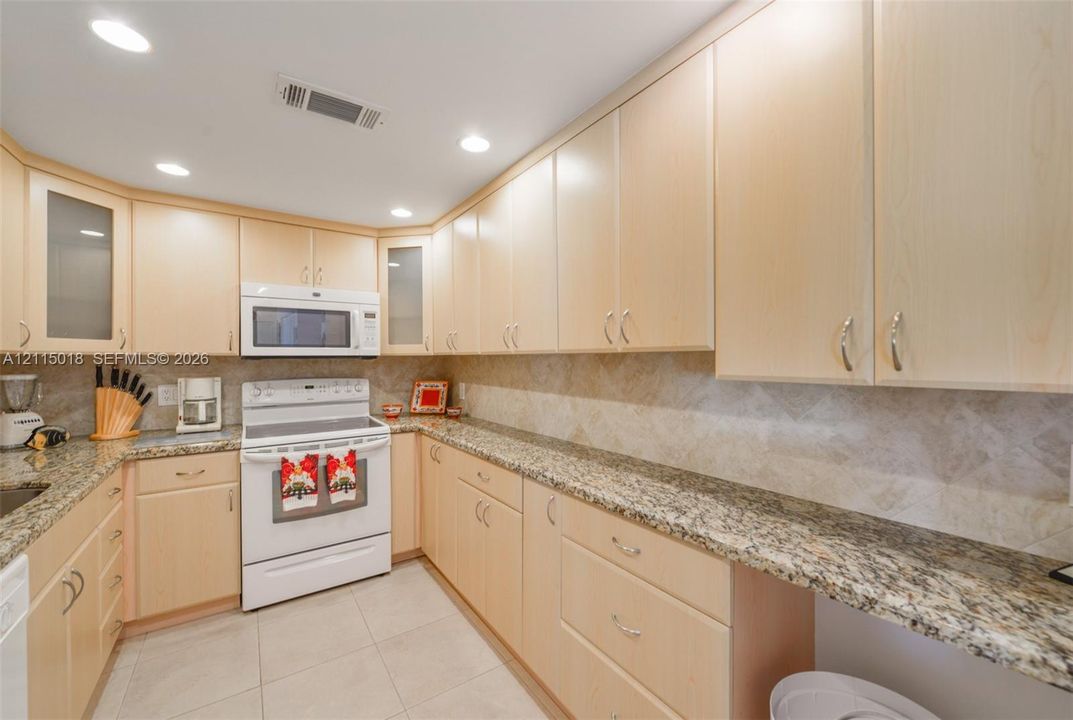 Kitchen featuring light-tone wood cabinetry, stone countertops, tiled backsplash, recessed lighting, and a white freestanding range