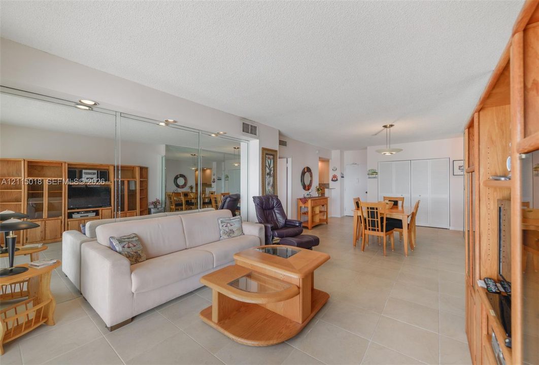 Open-concept interior featuring large-format ceramic tile flooring, mirrored wall panels, and built-in wood cabinetry