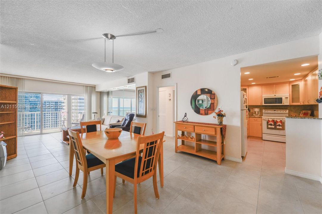 Open-concept area featuring light-toned tile flooring, recessed kitchen lighting, a modern multi-light pendant fixture, and a glass sliding door providing outdoor access