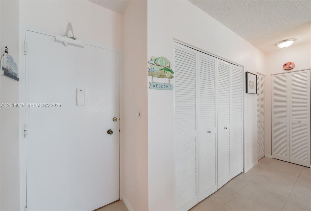 Solid core entry door with overhead hydraulic closer, louvered bi-fold closet doors, and ceramic tile flooring