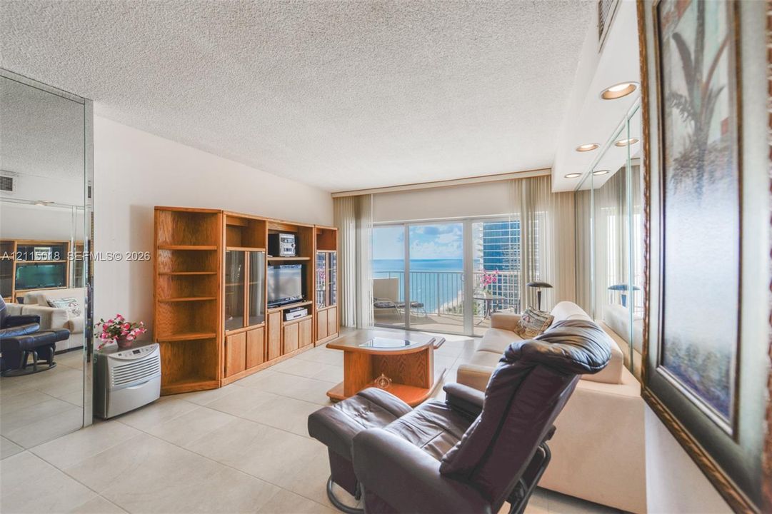 Large-format tile flooring, built-in wooden cabinetry, recessed ceiling lighting, wall-to-wall mirrored paneling, and sliding glass doors opening to a balcony