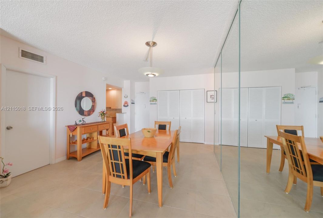 Large-format neutral floor tiling, floor-to-ceiling mirrored wall paneling, dual louvered-style closet doors, and a central tiered pendant light fixture