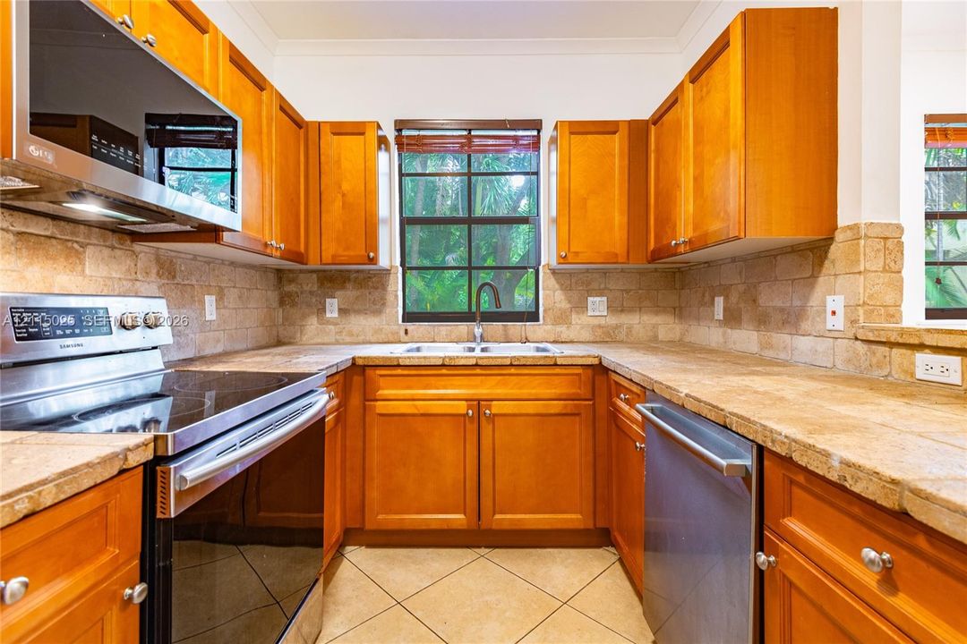 Kitchen featuring custom wood cabinetry, stone-tiled countertops, integrated stone backsplash, stainless steel appliances, and tile flooring